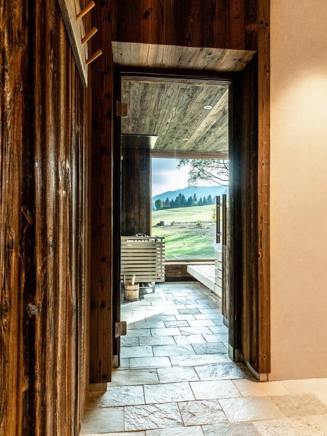 Blick durch die offene Glastür in die Sauna, Natursteinboden, dahinter das Fenster zur Landschaft