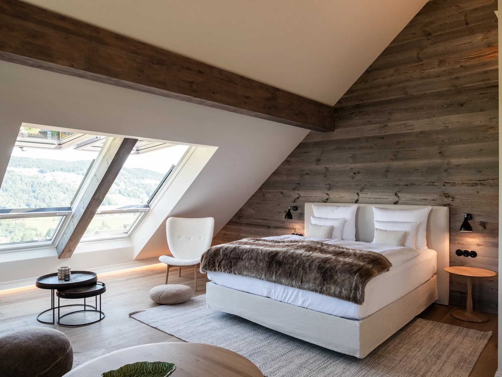 Übersicht der Suite Neun mit Bett vor der Altholzwand, Dachbalken und geöffnetem Dachfenster mit Ausblick